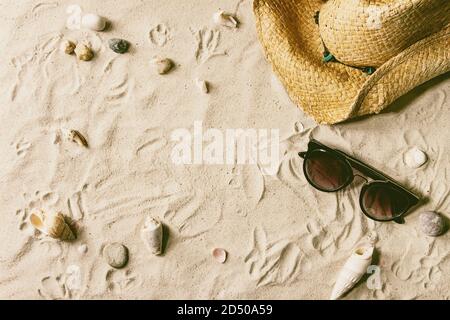 Tema estivo. Conchiglie, pietre di mare, occhiali da sole e cappello di paglia su sabbia bianca come sfondo. Disposizione piatta Foto Stock