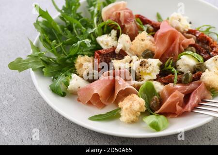 Rucola di insalata, prosciutto di Parma con pomodori secchi, fette di mozzarella, crostini, capperi, olio stagionato e spezie Foto Stock