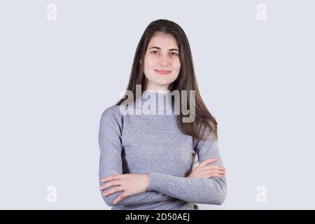 Ritratto sicuro giovane studentessa che guarda la fotocamera tenendo le mani incrociate su sfondo bianco con spazio per la copia. Ragazza studentesca che cerca Foto Stock