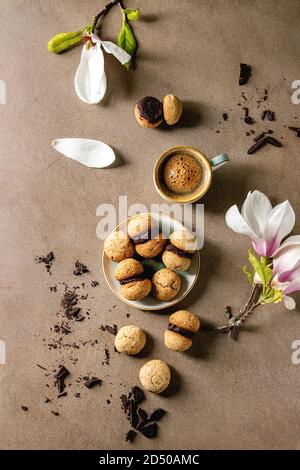 Baci di dama casalingo italiano biscotti di nocciole biscotti con crema di cioccolato servita nella piastra in ceramica con tazza di caffè espresso e di fiori di magnolia Foto Stock