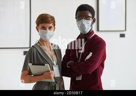 Vita in su ritratto di giovane donna tatuata che posa con l'uomo afroamericano entrambi indossando le maschere mentre progettano l'esposizione della galleria d'arte, spazio di copia Foto Stock