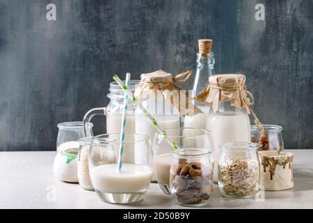 Varietà di non-dairy vegane senza lattosio dadi e granella di mandorle latte, nocciola, noce di cocco, riso, avena in bottiglie di vetro con gli ingredienti di cui sopra su white tabl Foto Stock