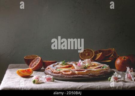 In casa la cheesecake con sangue siciliano arance, decorato da fiori commestibili, foglie di menta e zucchero in polvere servito nella piastra con arance tagliato in precedenza g Foto Stock