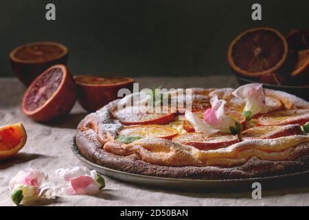 In casa la cheesecake con sangue siciliano arance, decorato da fiori commestibili, foglie di menta e zucchero in polvere servito nella piastra con arance tagliato in precedenza g Foto Stock