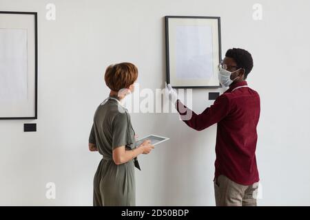 Indietro vista vita in su ritratto di manager donna che istruisce assistente indossare maschera mentre si pianifica la mostra galleria d'arte nel museo, copia spazio Foto Stock