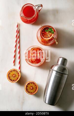 Cocktail ghiacciati all'arancia nel sangue in bicchieri, decorati da fetta di arance e menta fresca sugli spiedini, serviti con paglia retrò, caraffa di succo e shaker sopra Foto Stock