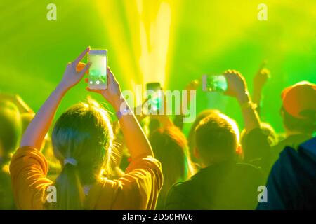 Adolescenti che scattano foto o registrano video di concerti di musica dal vivo con smartphone - vista posteriore. Illuminazione da palco colorata e luminosa. Vita notturna, tecnologia Foto Stock