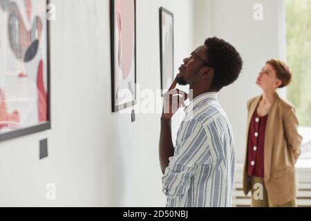 Vista laterale ritratto di un giovane afroamericano che guarda i dipinti mentre esplori la mostra della galleria d'arte moderna, copia spazio Foto Stock