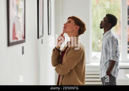 Vista laterale ritratto di elegante giovane donna guardando i dipinti mentre si esplora la mostra galleria d'arte moderna, spazio copia Foto Stock