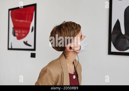 Vista laterale ritratto di giovane donna che guarda i dipinti e la maschera di indossare alla mostra galleria d'arte moderna, spazio copia Foto Stock