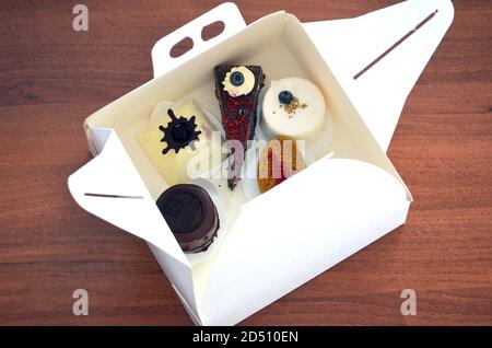 Elegante scatola bianca aperta piena di vari dolci e dessert su tavolo di legno. Celebrazione a casa. Take away. Foto Stock