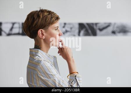 Grafica vista laterale ritratto di giovane donna tatuata guardando i dipinti alla mostra d'arte contemporanea, copia spazio Foto Stock