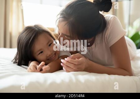 Primo piano madre asiatica baciando la bambina, sdraiata sul letto Foto Stock