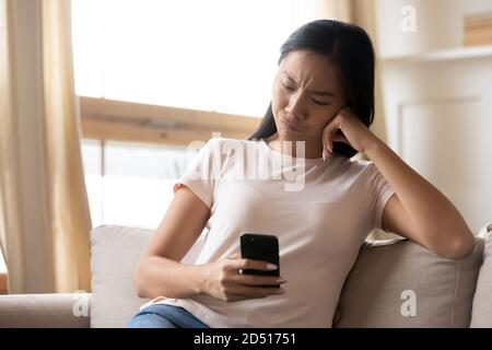 Infelice donna asiatica insoddisfatta che guarda lo schermo dello smartphone Foto Stock