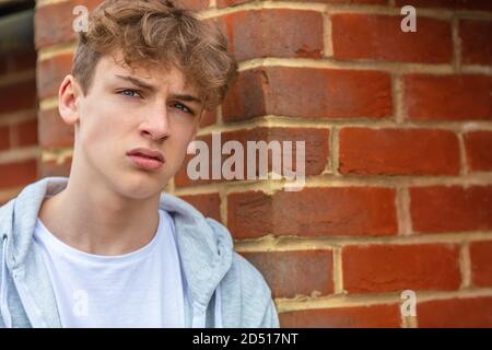 Un adolescente maschile serio che si appoggia all'esterno su una parete di mattoni che si indossa una felpa grigia nella città urbana Foto Stock