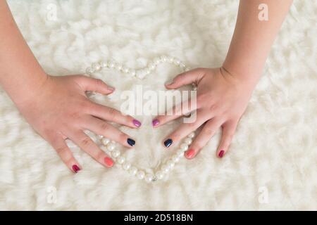 primo piano delle mani di giovane donna su un cuore di perla con unghie dipinte in diversi colori graziosi. due mani Foto Stock