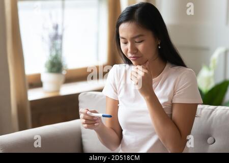 Infelice stressato giovane donna asiatica guardando il test di gravidanza Foto Stock