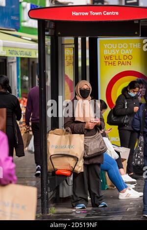 Londra, Regno Unito. 12 ottobre 2020. Una donna che indossa un facemask presso una fermata dell'autobus nel centro di Harrow. Si riferisce che cinque distretti londinesi hanno avuto più di 100 nuovi casi COVID-19 per 100,000 popolazione nella settimana fino all'8 ottobre: Richmond, Hackney, Ealing, Redbridge e Harrow. Mentre il Regno Unito sperimenta un aumento del numero di casi COVID-19 a livello nazionale, Boris Johnson, il primo ministro annuncia alla Camera dei Comuni un nuovo sistema di blocco locale a tre livelli per contrastare la diffusione del virus. Credit: Stephen Chung / Alamy Live News Foto Stock