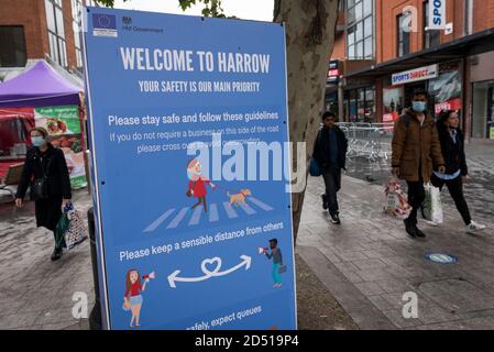 Londra, Regno Unito. 12 ottobre 2020. Gli acquirenti che indossano maschere passano davanti a un importante cartello sociale di distensione nel centro di Harrow. Si riferisce che cinque distretti londinesi hanno avuto più di 100 nuovi casi COVID-19 per 100,000 popolazione nella settimana fino all'8 ottobre: Richmond, Hackney, Ealing, Redbridge e Harrow. Mentre il Regno Unito sperimenta un aumento del numero di casi COVID-19 a livello nazionale, Boris Johnson, il primo ministro annuncia alla Camera dei Comuni un nuovo sistema di blocco locale a tre livelli per contrastare la diffusione del virus. Credit: Stephen Chung / Alamy Live News Foto Stock