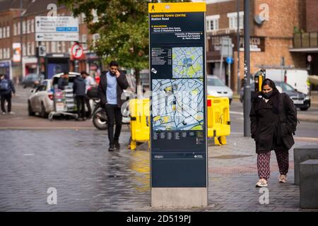 Londra, Regno Unito. 12 ottobre 2020. Una donna che indossa un facemask cammina su una mappa stradale nel centro di Harrow. Si riferisce che cinque distretti londinesi hanno avuto più di 100 nuovi casi COVID-19 per 100,000 popolazione nella settimana fino all'8 ottobre: Richmond, Hackney, Ealing, Redbridge e Harrow. Mentre il Regno Unito sperimenta un aumento del numero di casi COVID-19 a livello nazionale, Boris Johnson, il primo ministro annuncia alla Camera dei Comuni un nuovo sistema di blocco locale a tre livelli per contrastare la diffusione del virus. Credit: Stephen Chung / Alamy Live News Foto Stock