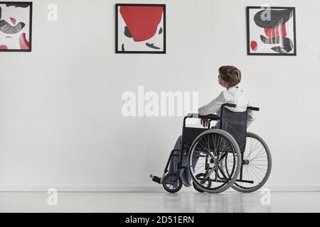 Ritratto grandangolare di giovane donna con sedia a rotelle guardando i dipinti nella galleria d'arte moderna, spazio di copia Foto Stock