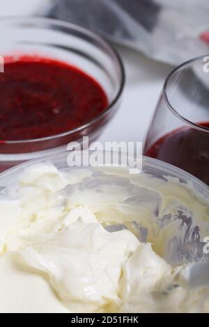 Dessert al formaggio cremoso con gelatina di lampone. Gli ingredienti sono disposti sulla superficie del tavolo. Decorato con biscotti, lamponi e menta. Foto Stock