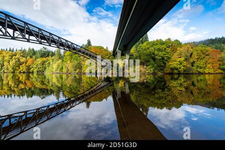 Pitlochry, Scozia, Regno Unito. 12 ottobre 2020. Colori autunnali su alberi che circondano Loch Faskally e passerella e A9 ponte stradale riflesso in acqua. In Pitlochry. Iain Masterton/Alamy Live News Foto Stock