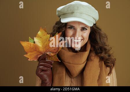 Ciao autunno. Ritratto di sorridente donna moderna di 40 anni in maglione con guanti in pelle e foglie di acero giallo autunno isolate su beige. Foto Stock
