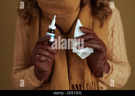 Ciao novembre. Closeup su donna di mezza età in sciarpa con fazzoletti di carta, spray nasale e guanti in pelle su sfondo di bronzo. Foto Stock