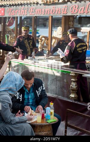 Una coppia turca che mangia un sandwich di pesce il famoso cibo di strada Balik Ekmek accanto al Corno d'Oro a Istanbul. Foto Stock