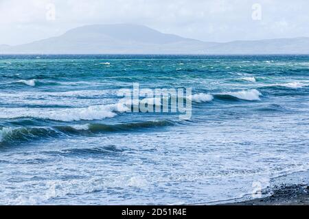 Onde che rotolano verso la riva in una giornata ventosa in Clew Bay con vista sull'isola di Clare dalla pietra spiaggia a Killadoon sul giro di Killeen passeggiate vicino Louis Foto Stock