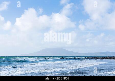 Onde che rotolano verso la riva in una giornata ventosa in Clew Bay con vista sull'isola di Clare dalla pietra spiaggia a Killadoon sul giro di Killeen passeggiate vicino Louis Foto Stock