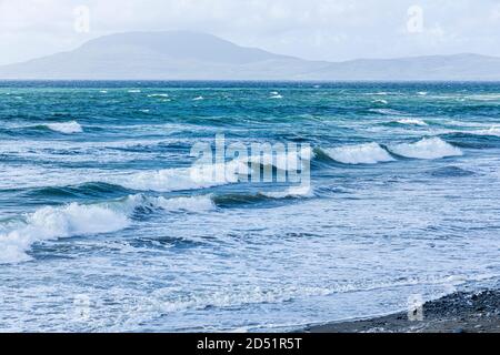 Onde che rotolano verso la riva in una giornata ventosa in Clew Bay con vista sull'isola di Clare dalla pietra spiaggia a Killadoon sul giro di Killeen passeggiate vicino Louis Foto Stock