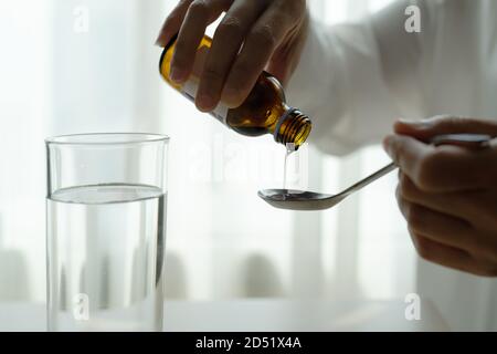 La donna versa manualmente le medicine o tosse sciroppo da bottiglia a cucchiaio. Il concetto di assistenza sanitaria Foto Stock