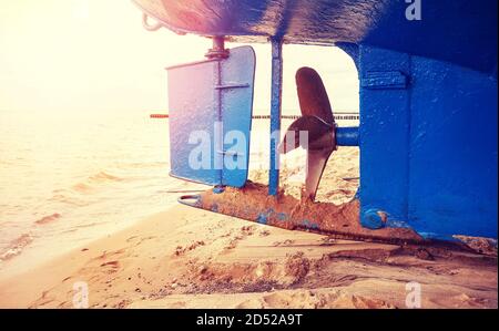 Timone di barche da pesca e elica su una spiaggia al tramonto, fuoco selettivo, tonalità di colore applicato. Foto Stock