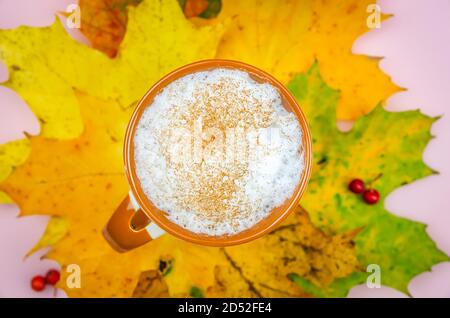 Tazza di cappuccino con cannella su foglie di acero luminoso da vicino, vista dall'alto. Splendido sfondo autunnale con una tazza di caffè Foto Stock
