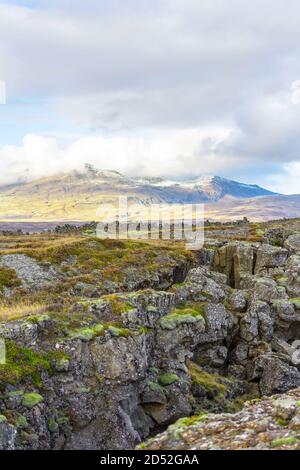 Un canyon mussoso di fronte, sullo sfondo un grande ghiacciaio o una montagna nascosta da nuvole, toccata dalla luce calma del sole, a Thingvellir, Islanda. Foto Stock