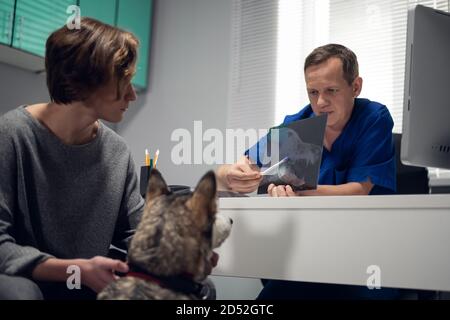 Una giovane donna in un check-up del suo cane da Husky, seduto presso l'ufficio dei veterinari, discutendo i risultati dei raggi X con il doc. Foto Stock