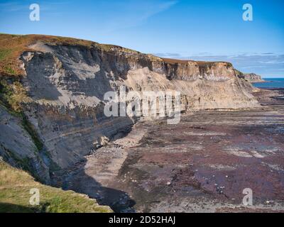 A nord di Robin Hood's Bay nello Yorkshire, Regno Unito, la bassa marea rivela l'altopiano della formazione di Cleveland Ironstone sotto le scogliere costiere di Whitby Mudstone Foto Stock