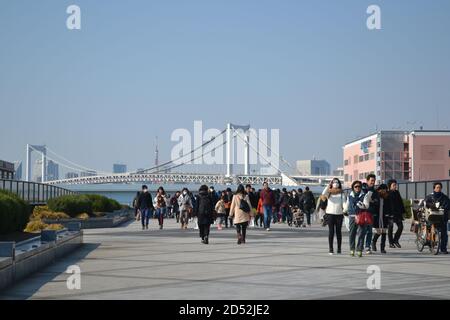 Tokyo, Japan-2/26/16: Cieli azzurri e folle di persone che camminano intorno a Odaiba Tokyo. Dietro di loro, il Ponte dell'Arcobaleno e la Torre di Tokyo. Foto Stock