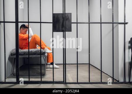 Cella solitaria con un criminale in un accappatoio arancione in una prigione asiatica. Spazio di copia. Emozioni tristi di un ragazzo giovane Foto Stock