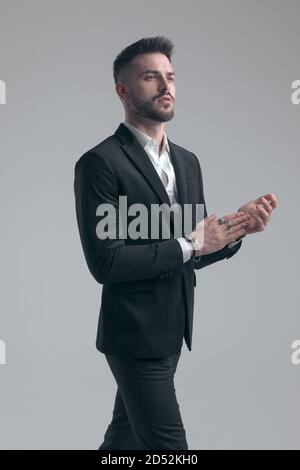 Uomo orgoglioso ed elegante che si aggrappano e si guarda lontano, indossando un vestito mentre si cammina su sfondo grigio studio Foto Stock