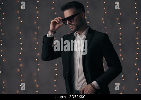 Modello di moda sicuro togliere i suoi occhiali da sole e guardare via mentre si sta in piedi su sfondo grigio studio con luci Foto Stock