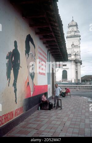 Sandjnista murale rivoluzionario con immagine di leader caduto, Carlos Fonseca e citazione da lui, a Granada, Nicaragua nel periodo Sandinista, 1986, con un uomo shoeshine di fronte al muro. Foto Stock