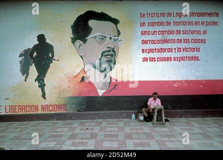 Sandjnista murale rivoluzionario con immagine di leader caduto, Carlos Fonseca e citazione da lui, a Granada, Nicaragua nel periodo Sandinista, 1986, con un uomo shoeshine di fronte al muro. Foto Stock