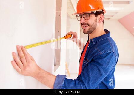 Ritratto di giovane uomo con nastro di misurazione mentre si lavora sul sito in costruzione. Foto Stock