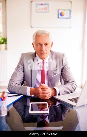 Banca di successo direttore imprenditore seduto alla scrivania in ufficio e guardando la fotocamera. Foto Stock