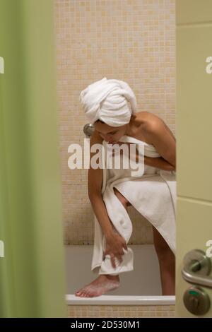 Scatto verticale di una donna caucasica in accappatoio e asciugamano sulla testa dopo bagno che si asciuga Foto Stock