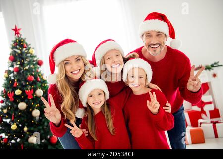 Foto ritratto di divertente famiglia amichevole indossare caldo rosso festivo ponticelli e copricapo che si preparano per la vigilia di natale vicino all'albero di natale decorazioni con v Foto Stock