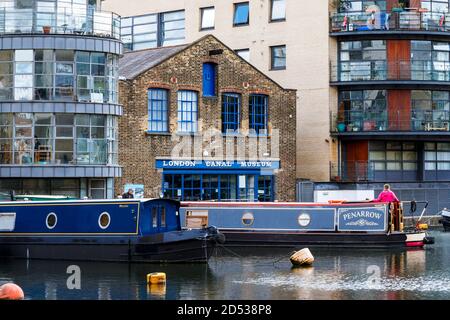 Una donna in un cappotto rosa ruba una narrowboat nel suo ormeggio fuori dal London Canal Museum, Battlebridge Basin, King's Cross, Londra, Regno Unito Foto Stock